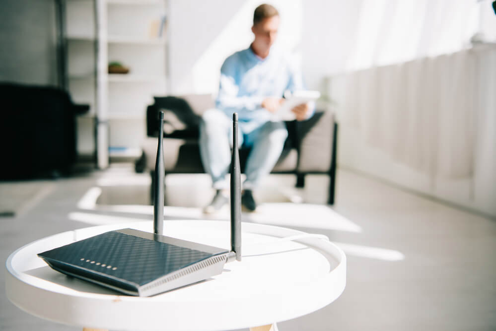 A picture of a wifi router with someone in the background sitting down with a device in hand.